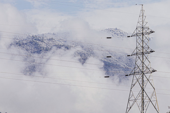 Powerlines in front of a snowy and foggy mountain.
